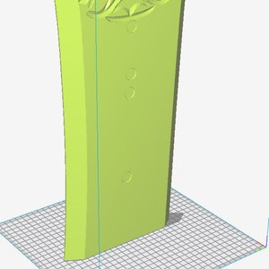 May include: A light green, stylized, rectangular object with a decorative floral design at the top and three circular indentations. The object is standing upright on a grid.