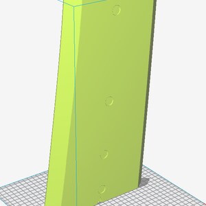 May include: A light green, rectangular object with a slanted edge and three circular indentations. Two small holes are at the top. The object is set against a grid background.