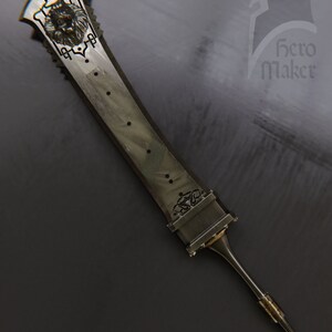 May include: A large, ornate sword with a wide, rectangular blade. The blade features a lion's head design and decorative etchings. The handle is long and slender, with gold-colored accents. The sword has a dark, metallic finish.