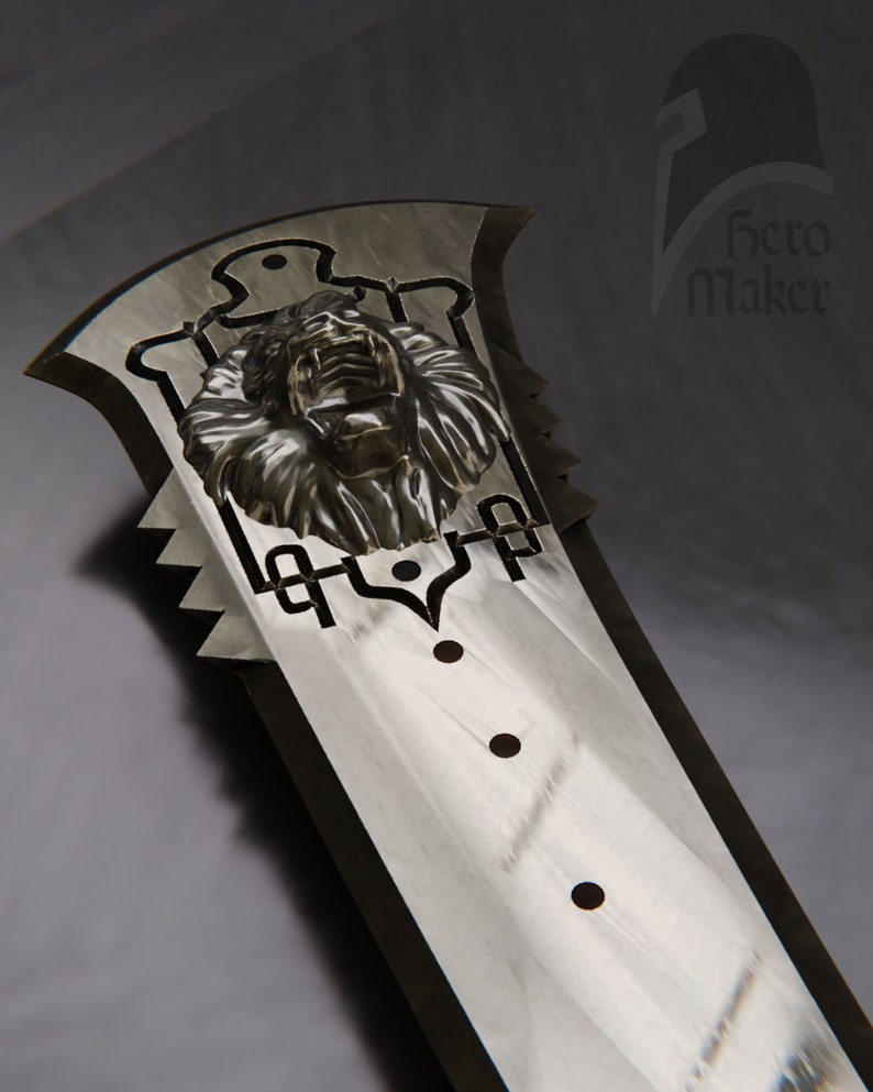 May include: A large, silver-colored sword with a detailed lion's head emblem near the hilt. The blade has a series of decorative cutouts and three dark circular accents. The Hero Maker logo is visible in the upper right corner.