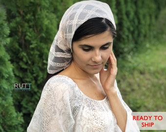 May include: A white lace head covering with a delicate pattern. The head covering is worn by a person with dark hair and is styled to cover the head and neck.
