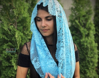 May include: A light blue lace veil with a delicate floral pattern. The veil is draped over a person's head and shoulders.