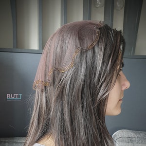 May include: A brown sheer head covering with a scalloped edge decorated with gold beads.