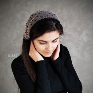 以下が含まれることがあります： 黒のタートルネックのシャツと、黒と白のドット柄のシアーなヘッドバンドをつけた、長い黒髪の女性。ヘッドバンドには黒いレースのトリムが施されています。