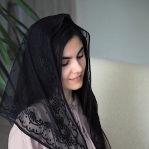 May include: A black lace veil with a delicate floral pattern. The veil is draped over a person's head and shoulders.