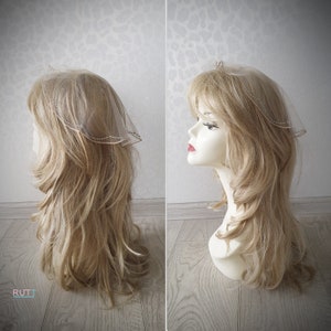 Puede incluir: Un velo blanco transparente con un borde de cuentas. El velo se lleva en un maniquí con el pelo largo y rubio.