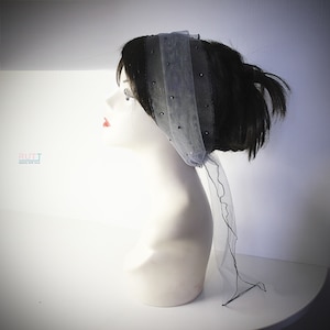 May include: A black and gray headband with a sheer fabric and black bead accents. The headband is tied in a knot at the back of the head.