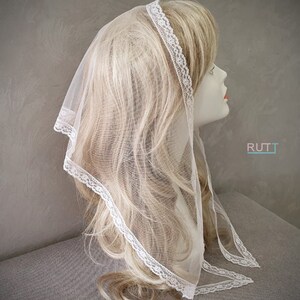 Puede incluir: Velo de encaje blanco transparente con un delicado borde de encaje. El velo est&aacute; drapeado sobre una cabeza de maniqu&iacute; con cabello rubio.