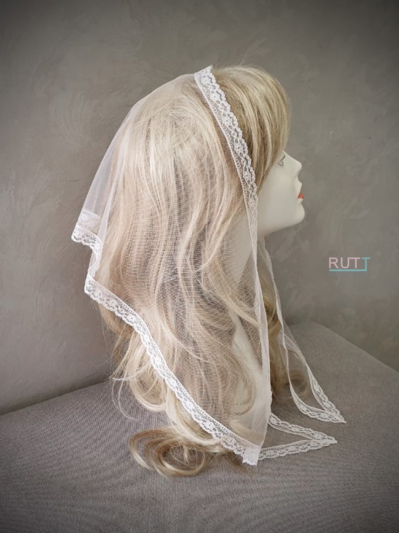Puede incluir: Velo de encaje blanco transparente con un delicado borde de encaje. El velo est&aacute; drapeado sobre una cabeza de maniqu&iacute; con cabello rubio.