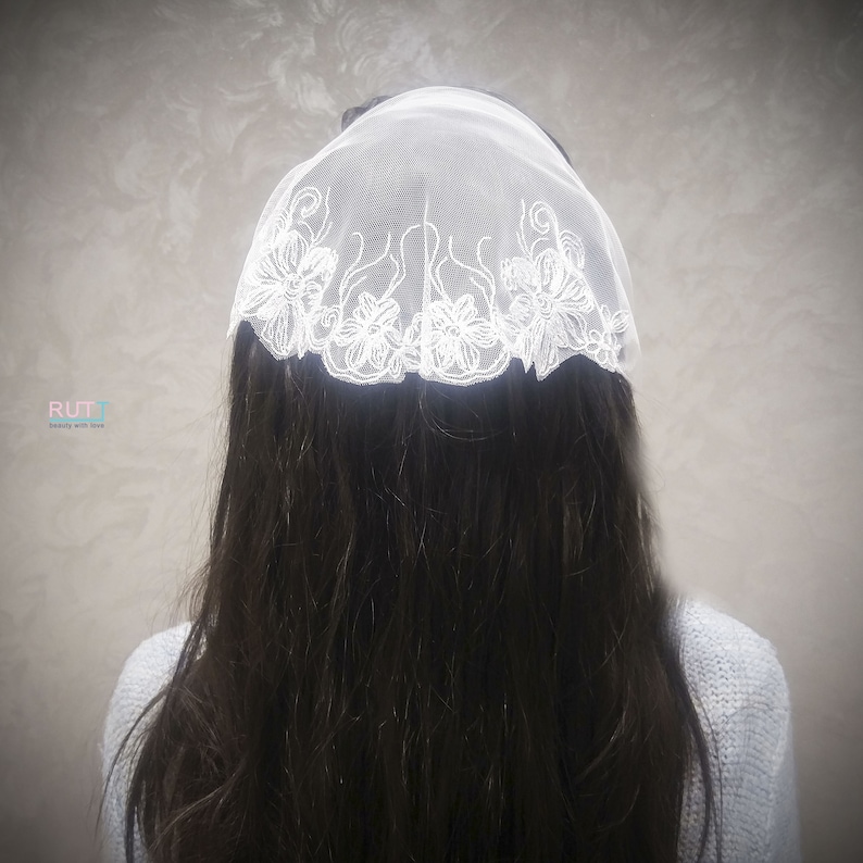 Puede incluir: Un velo de encaje blanco con bordados florales. El velo se lleva en la cabeza y cubre el cabello.