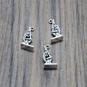 Può includere: Tre ciondoli a forma di microscopio in argento con un design dettagliato. I ciondoli sono perfetti per aggiungere un tocco scientifico a gioielli o artigianato.