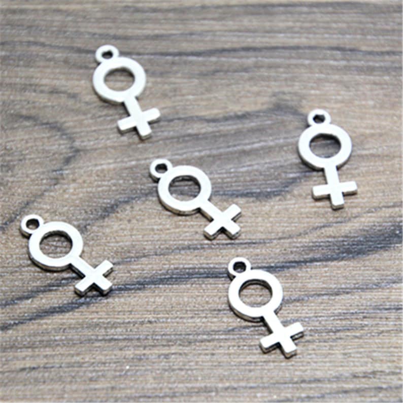 Puede incluir: Cinco dijes de metal plateado en forma de s&iacute;mbolo femenino.
