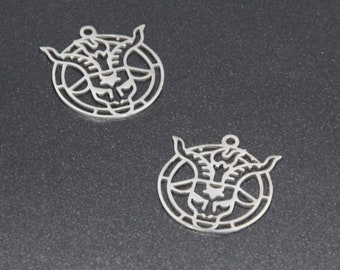 Könnte beinhalten: Zwei silberne Metallanhänger in Form eines Ziegenkopfes in einem Kreis. Der Ziegenkopf ist nach vorne gerichtet mit Hörnern und einem Bart. Der Kreis hat ein Pentagramm-Design.