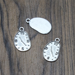 Peut inclure: Trois breloques en métal argenté en forme d'horloge fondante. Les breloques ont un trou en haut pour être attachées à un collier ou un bracelet.