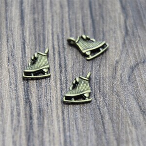 Pode incluir: Três pingentes de patins de gelo em tom dourado antigo. Os pingentes são detalhados com uma superfície texturizada e um laço para prender a um colar ou pulseira.