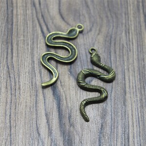 May include: Two antique gold-toned snake charms. The charms are detailed with scales and have a loop at the top for attaching to jewelry.
