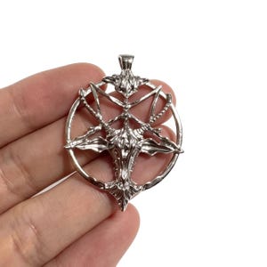 Może przedstawiać: Srebrny wisiorek z szczegółowym przedstawieniem symbolu Baphometa w okręgu. Wisiorek ma skomplikowane detale i polerowane wykończenie, odpowiedni do biżuterii lub alternatywnej mody.