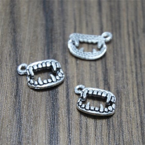 May include: Three silver charm pendants shaped like a set of teeth. The charms are detailed with sharp points and are perfect for adding a spooky touch to jewelry.