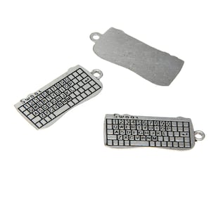 Puede incluir: Tres abalorios plateados con un diseño de teclado. Los abalorios tienen forma de teclado y tienen los números del 1 al 9, las letras QWERTYUIOP, ASDFGHJKL y ZXCVBNM, y las palabras "Swac" y "Swaac" impresas en ellos.