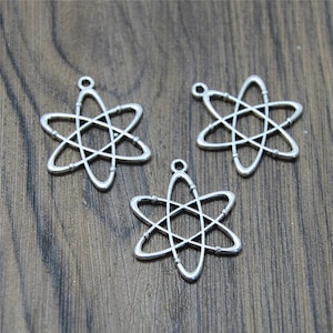 Puede incluir: Tres colgantes de átomo de plata con un diseño detallado. Los colgantes tienen la forma de una estrella con un círculo en el centro y líneas que irradian desde el círculo.