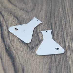 Op de afbeelding: Twee zilveren metalen hangers in de vorm van bekers met een klein hartje dat uit elk is uitgesneden.