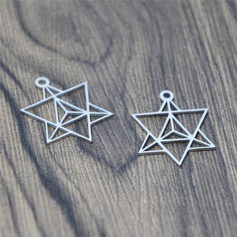 May include: Two silver metal star-shaped charms with a geometric design. The charms have a hole at the top for attaching to a necklace or bracelet.