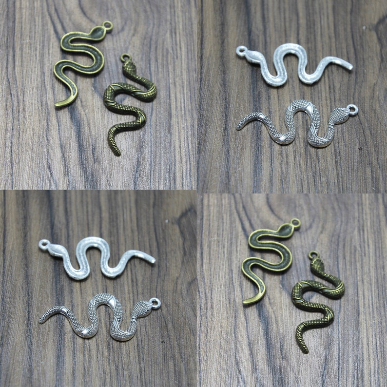 May include: Four silver and bronze snake charms with a textured surface. The charms are in the shape of a snake with a curled tail. The charms are on a wooden surface.