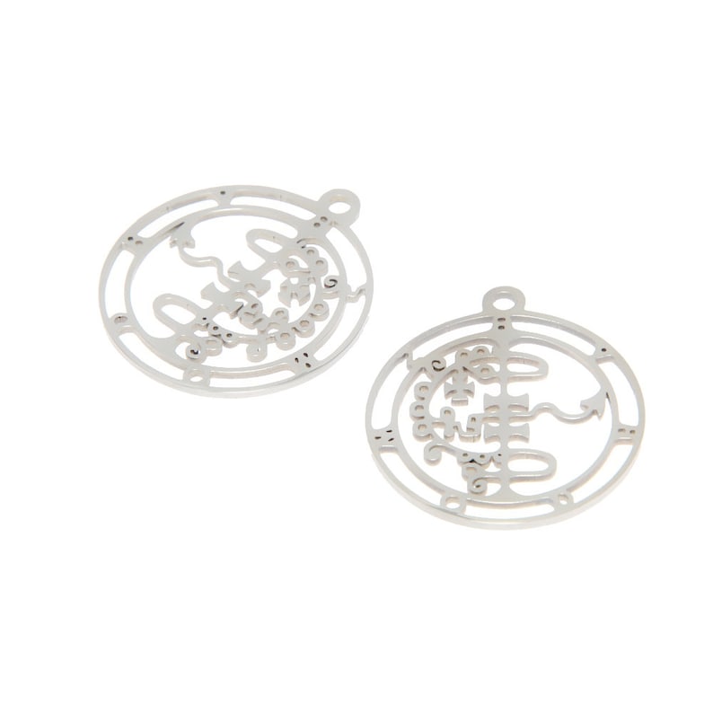 May include: Two silver metal charms with intricate circular designs. Each charm features a stylized image of a creature with a long tail and a series of concentric circles.