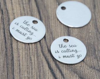 May include: Two silver round metal charms with the text "the sea is calling... i must go" engraved on them.