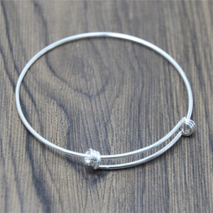 May include: A silver bangle bracelet with a simple design. The bracelet is made of a thin wire and has a small, round clasp.