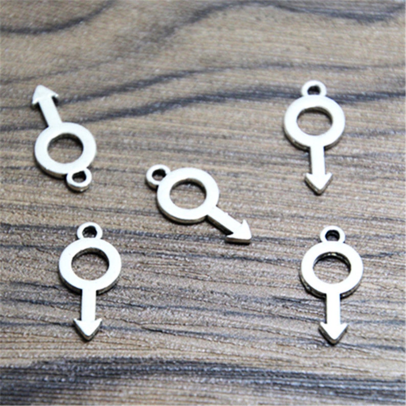May include: Five silver metal charms in the shape of the male symbol. Each charm has a circle with an arrow pointing down.