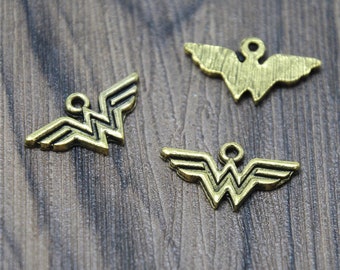 Puede incluir: Tres abalorios de metal de color dorado en forma del logotipo de Wonder Woman. Los abalorios están sobre una superficie de madera.