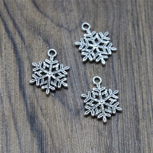 Op de afbeelding: Drie zilveren sneeuwvlokcharms met ingewikkelde details. De charms zijn perfect om een ​​toets van winterse magie toe te voegen aan sieraden of knutselwerk.