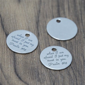 May include: Two silver round charms with a hole at the top. One charm has the text "when I am afraid I put my trust in you. Psalm 563" engraved on it. The other charm is blank.