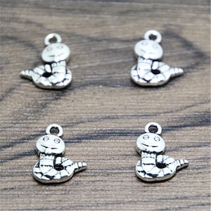 May include: Four silver charm pendants shaped like snakes with a smiling face. The snake charms are coiled and have a textured surface.
