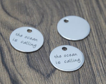 May include: Three silver metal round charms with a hole at the top. Two of the charms have the text "the ocean is calling" engraved on them. The third charm is blank.