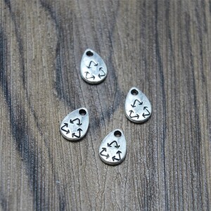 May include: Four silver teardrop-shaped charms with a black recycling symbol design.