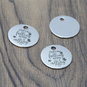 May include: Two silver metal round charms with a hole at the top. One charm has the text "Leaves are falling, autumn is calling" with a leaf design. The other charm is blank.