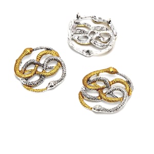 May include: Three silver and gold snake knot charms. The charms are in the shape of two snakes intertwined in a circle. The snakes are silver with gold accents.