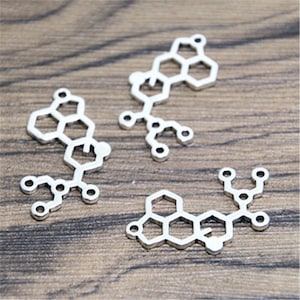 May include: Four silver metal charms shaped like chemical structures. The charms are intricate and detailed, with multiple hexagonal and circular shapes.