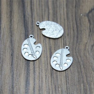 May include: Three silver-toned metal charms shaped like artist's palettes with paintbrush details.