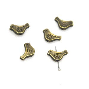 May include: Five antique gold-coloured bird-shaped beads with a swirl design. The beads are approximately 2.5 cm long and are ideal for jewellery making.