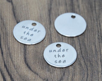May include: Three silver metal round charms with a hole at the top. Two of the charms have the text "under the sea" engraved on them. The third charm is blank.