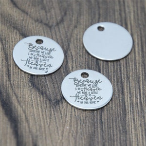 May include: Two silver metal round tags with a hole at the top. The tag on the left has the text "Because someone we love is in Heaven we have a little bit of Heaven in our home." The tag on the right has the same text but with a slightly different font.