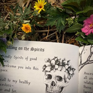 Op de afbeelding: Een zwart-witte illustratie van een schedel met een bloemenkrans. De schedel glimlacht en heeft een bloemenkrans om zijn hoofd. De tekst "Calling on the Spirits" is zichtbaar bovenaan de pagina. De tekst "Kindly Spirits of good race, I welcome you into this space." is zichtbaar onder de schedel.