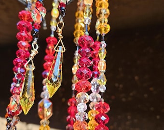 May include: Close-up of a decorative beaded hanging ornament. The ornament features strands of faceted beads in shades of red, yellow, orange, and clear. Some strands have dangling crystal-like pendants.