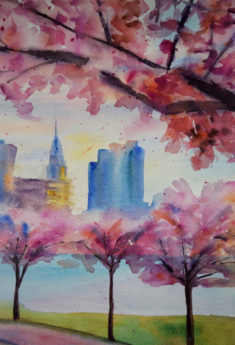 以下が含まれることがあります： 水彩画は、ピンクの桜の木が前景にあり、街の景色を描いています。街の建物は青と紫の色合いで描かれており、桜の花は鮮やかなピンクです。空は柔らかな青で、黄色のヒントがあります。