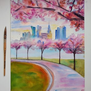 以下が含まれることがあります： 水彩画で描かれた街並みの風景画。ピンクの桜の花が咲き乱れる木々が前景にあり、街へと続く曲がりくねった道が描かれている。