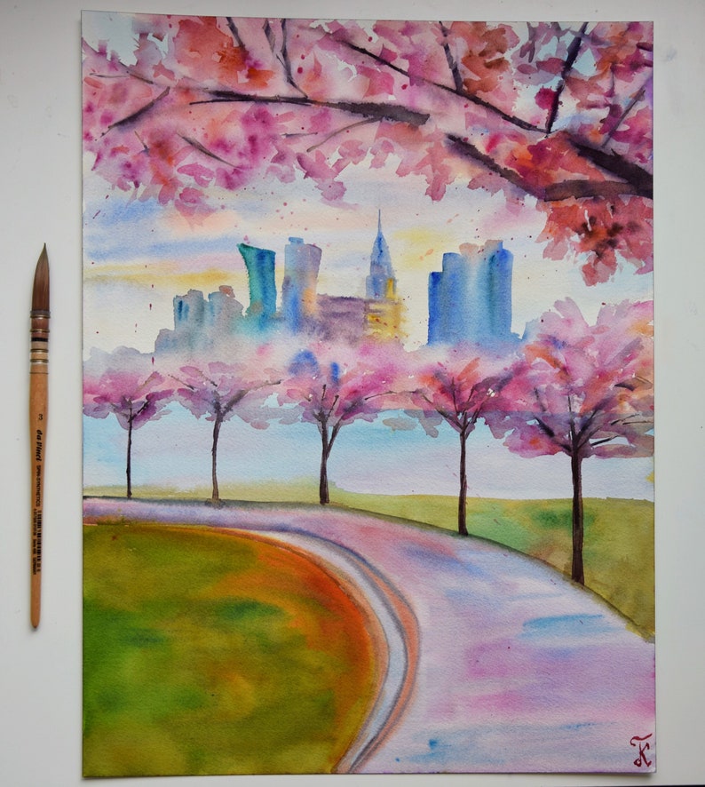 以下が含まれることがあります： 水彩画で描かれた街並みの風景画。ピンクの桜の花が咲き乱れる木々が前景にあり、街へと続く曲がりくねった道が描かれている。