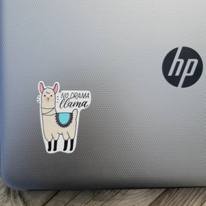 May include: A white llama sticker with a blue and black patterned saddle. The sticker has the text "NO DRAMA llama" on it.